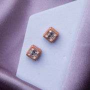 A pair of rose gold glittering silver stud earrings placed on a white surface with a blurred background.